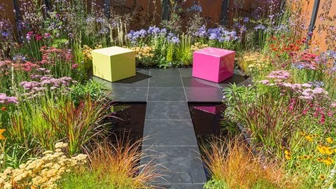 A stone walkway leads across two reflective pools to a seating area, featuring colourful cubes which are both decorative and functional.