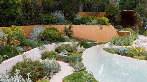 An arresting contemporary style garden, featuring dramatically curved beds with a sweeping central water feature, leading the eye through Mediterranean-style planting to an enclosed seating area