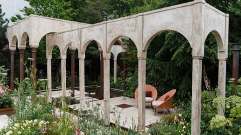 Soft shade-tolerant naturalistic planting surrounds the architectural arched structure central to the garden, with mature trees of pine, conifer and cedar lining the boundary