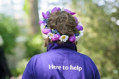 A person in a purple t-shirt reading ‘here to help’ and a flower crown