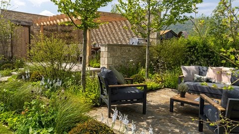 From dining area to informal seating, and a wild meadow filled with ragged robin, this garden flows alongside a gentle brook, with <i>Cirsium</i> punching through the soft planting