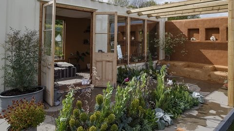 The setting for an artist's studio, the interior (complete with artist's easel) looks out over a space of mainly green planting, alongside natural, neutral tones of hard landscaping