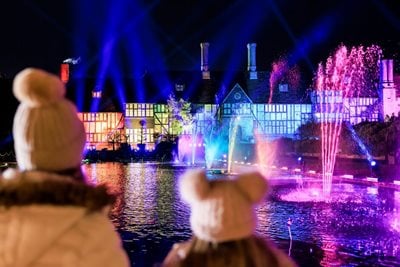 An adult and a child watch the illuminated Old Laboratory and fountains at RHS Wisley