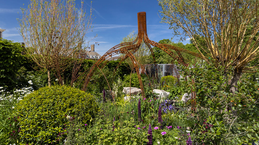 Garden with metal structure rising out its centre: 9 iron bars shaped like mangrove tree roots.