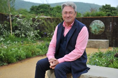 Alan Titchmarsh sitting on stone in a garden