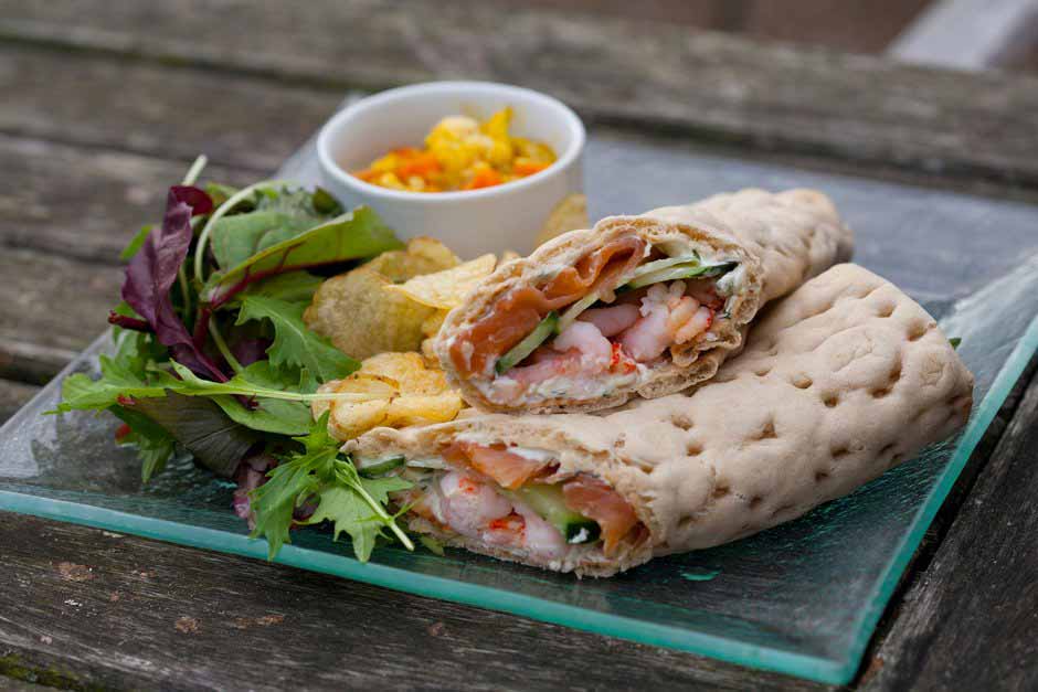 A prawn sandwich and a salad are seen on a plate sitting on a rustic wooden table