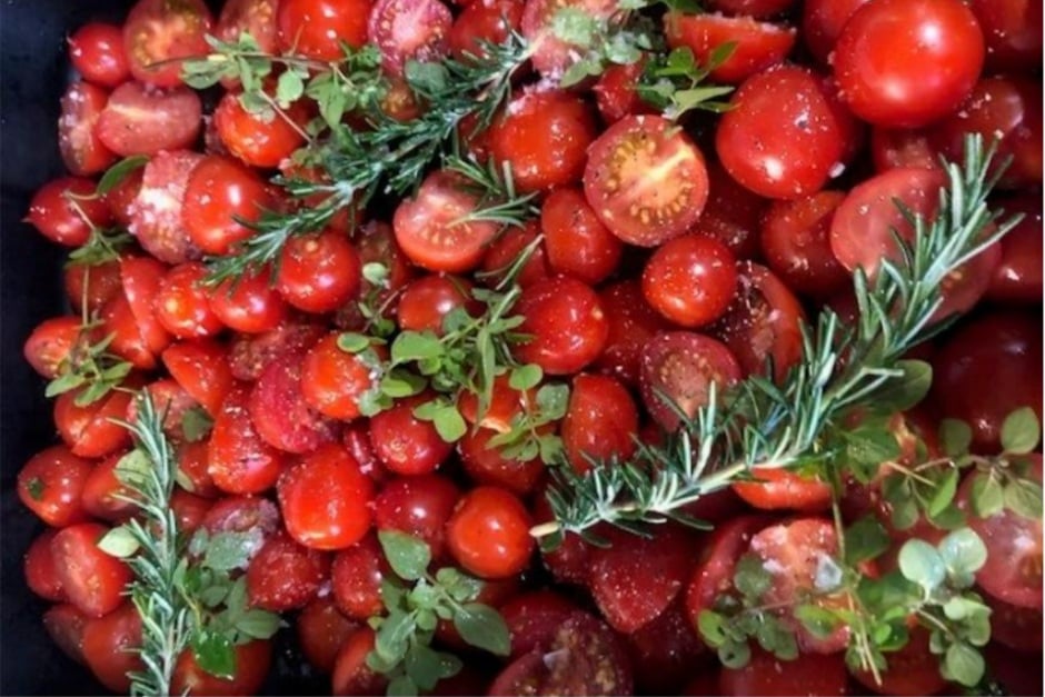 A roasting tray of seasoned cherry tomatoes with rosemary and oregano, by Anne Adam
