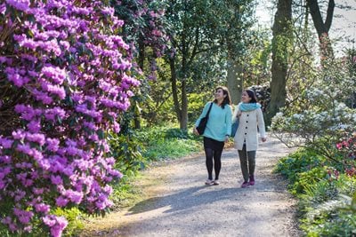 A mum and daughter visiting RHS Hyde Hall in spring, with flowering rhododendrons