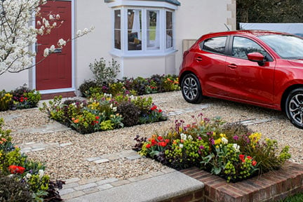 Although there is room to park, plants feature heavily in this garden. There is a small tree, a diverse range of perennial plants in the beds and permeable gravel paving. However, there's still room for climbers up the walls.