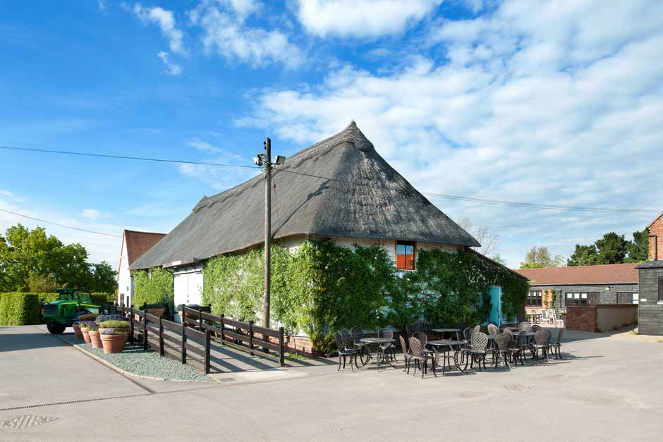 A wide view of a rustic thatched barn and surrounding courtyard on a sunny day
