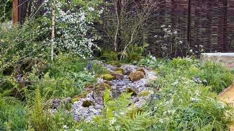 Planting in hues of green, white and blue surrounds simple stone seating where the sound from a gentle stream creates a tranquil environment for reflection